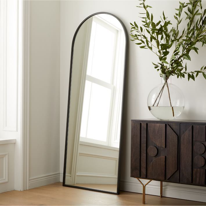Modern home interior showing a tall arched mirror and dark wood luxury furniture for how to choose luxury furniture for home