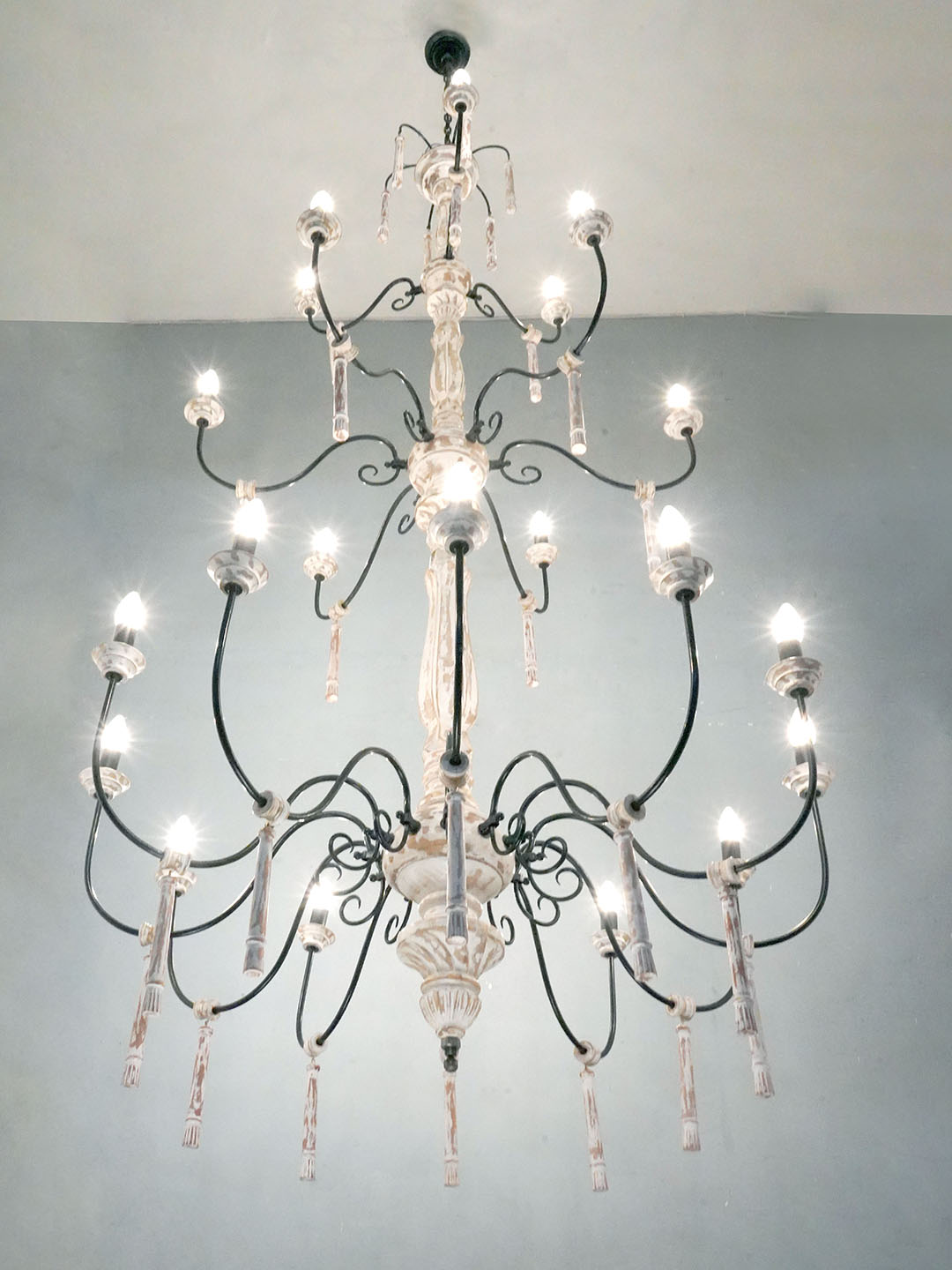 Chic French Country 21 Lights 3 Tier Rustic White Wood and Wrought iron Candelabra Chandelier with lights on and placed in a home